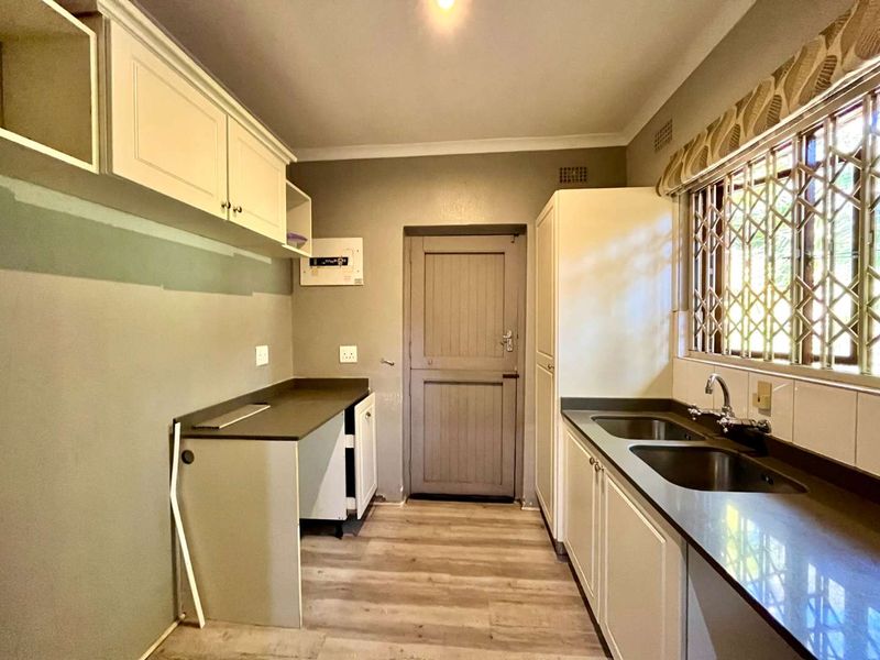 A functional scullery area featuring double stainless steel sinks, laminate countertops, ample built-in cabinetry, and durable laminate flooring.