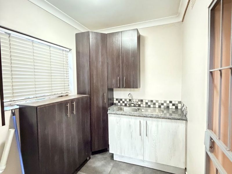 A functional laundry room featuring dark and light wood-finish cabinetry, a stainless steel sink with granite countertop, and durable tiled flooring.
