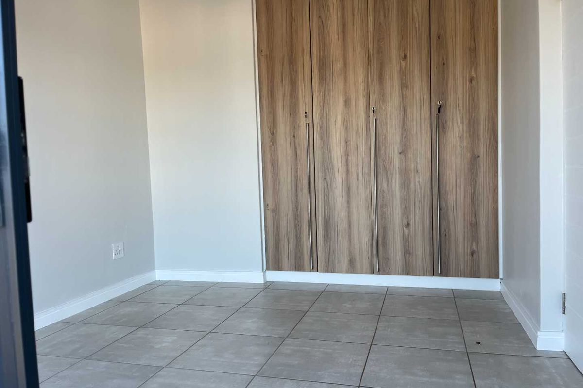 A clean, empty bedroom featuring modern wood-finish built-in cupboards and neutral tiled flooring, providing a versatile space ready for personalization.