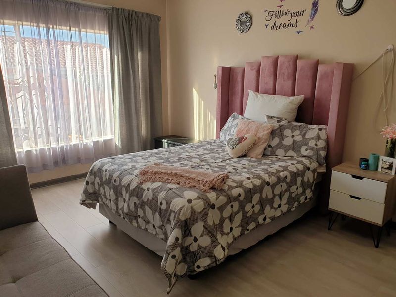 A well-lit bedroom featuring light-toned laminate flooring and large windows with curtain rails, providing a comfortable and functional living space.