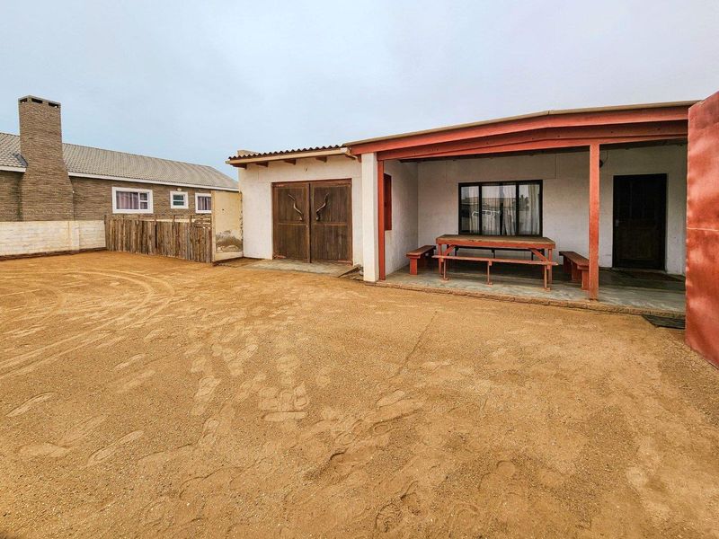 Rear exterior view featuring a covered patio area, timber double doors, and a large open sandy yard space.