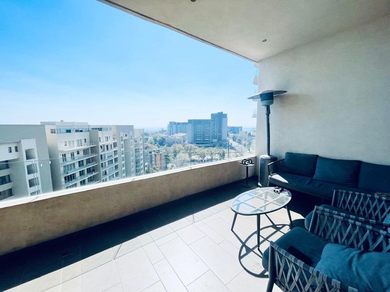 Spacious covered balcony featuring modern tiled flooring, a sleek glass balustrade, and expansive urban views.