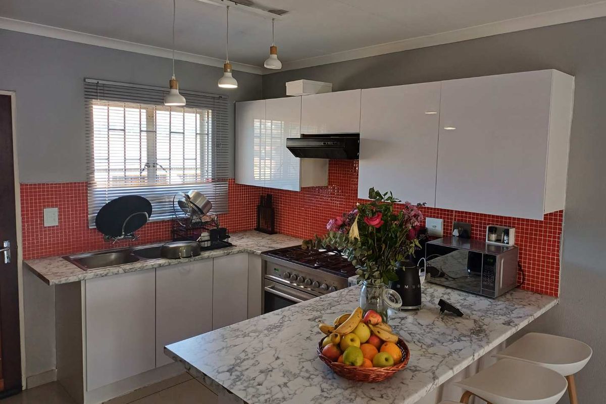 Modern kitchen featuring white high-gloss cabinetry, marble-look countertops, a gas stove with extractor fan, and a vibrant red mosaic tile backsplash.