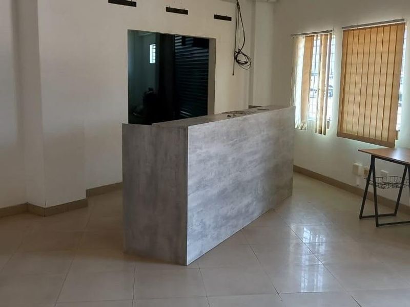 An open-plan office space featuring a central reception desk, tiled flooring, and vertical window blinds.