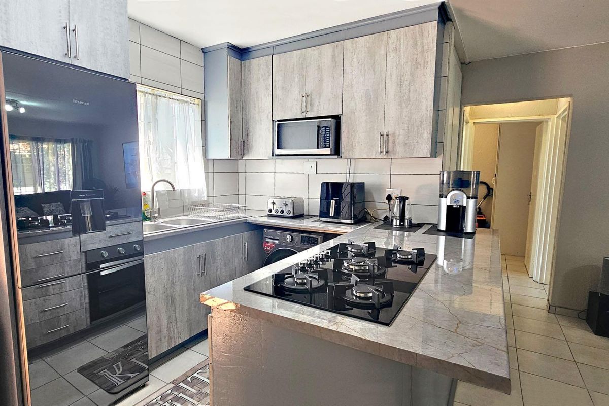 Modern kitchen featuring stone-look countertops, built-in gas hob, integrated cabinetry, and tiled flooring in an open-plan layout.