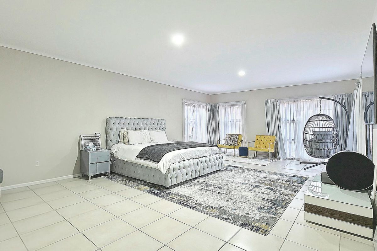 Spacious bedroom featuring neutral wall tones, large format floor tiles, recessed lighting, and sliding glass doors providing access to the exterior.