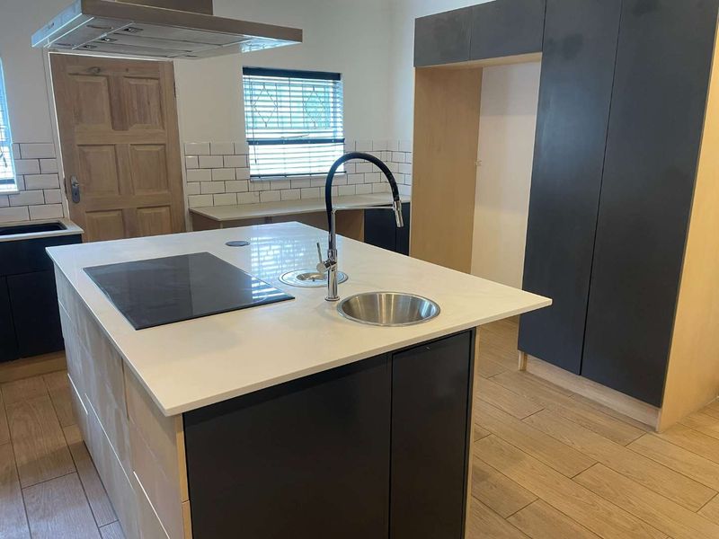 Modern kitchen featuring a central island with a built-in hob, sink, and sleek cabinetry, complemented by subway tile backsplashes and wood-look tiled flooring.