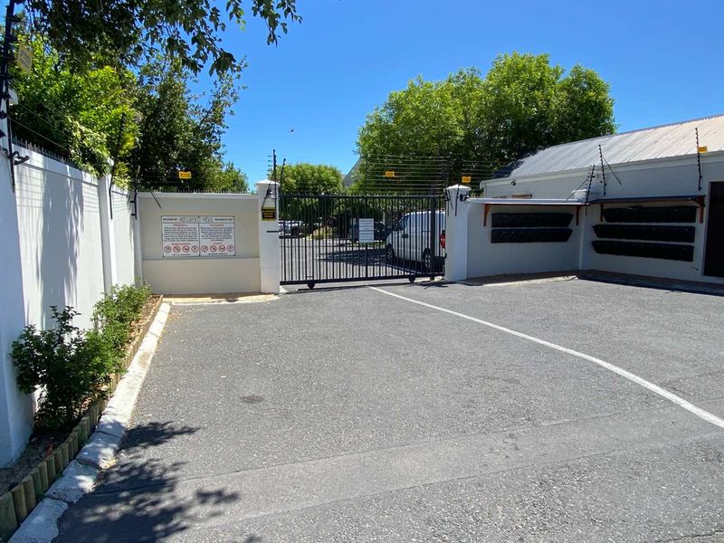 Secure gated entrance to the townhouse complex featuring asphalt driveway, boundary walls with electric fencing, and wall-mounted post boxes.