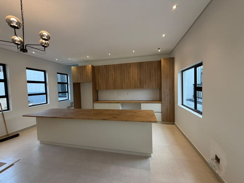 Modern kitchen featuring a central island, wood-finish cabinetry, recessed lighting, and large windows, providing a bright and contemporary space ready for final touches.