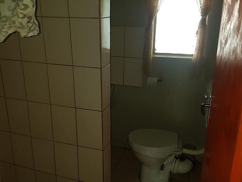 A functional bathroom featuring tiled walls and flooring, a standard toilet, and a shower enclosure, requiring cosmetic updates to modernize the space.