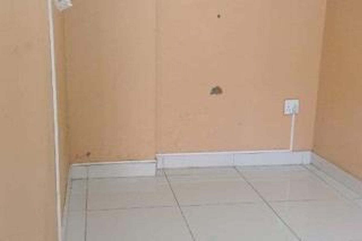 A small, empty room featuring tiled flooring and plain walls with visible surface wear and exposed electrical wiring.