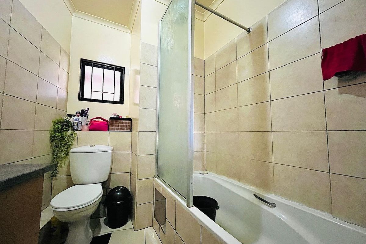 A functional bathroom featuring a bathtub with a glass shower screen, tiled walls and flooring, and a standard toilet.