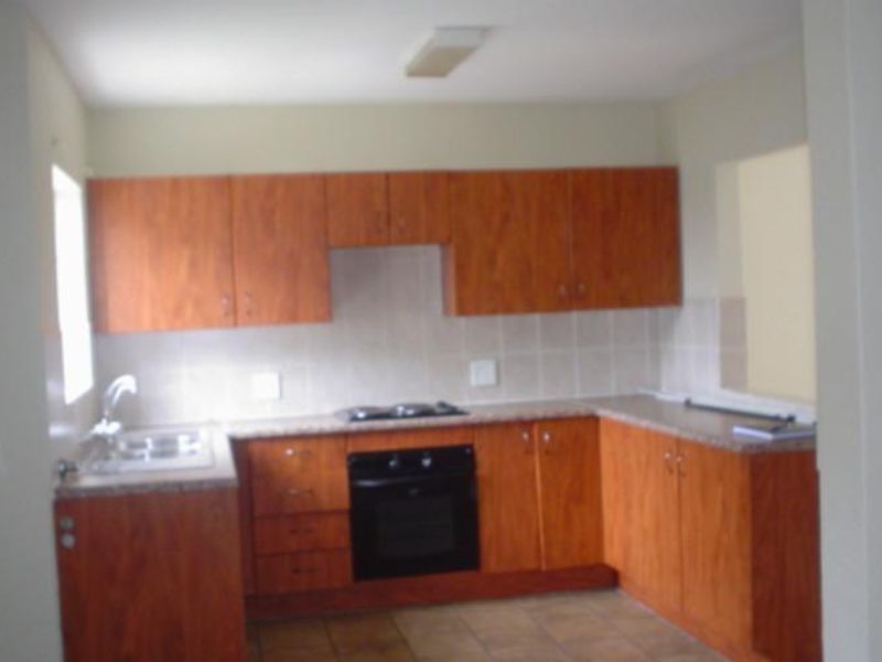 A functional kitchen featuring wood-look laminate cabinetry, built-in oven, hob, tiled backsplash, and laminate countertops with a stainless steel sink.