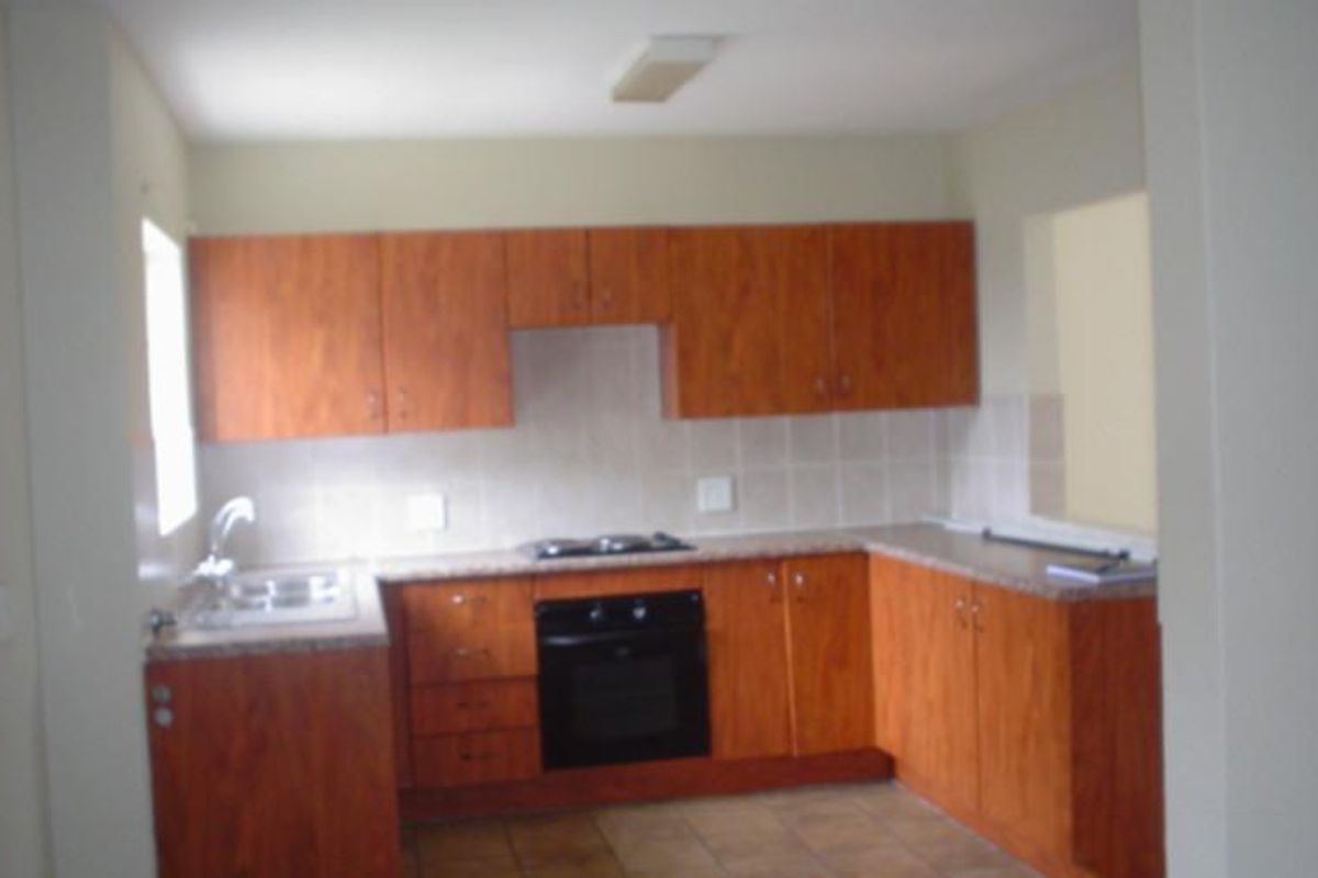 A functional kitchen featuring wood-look laminate cabinetry, built-in oven, hob, tiled backsplash, and laminate countertops with a stainless steel sink.