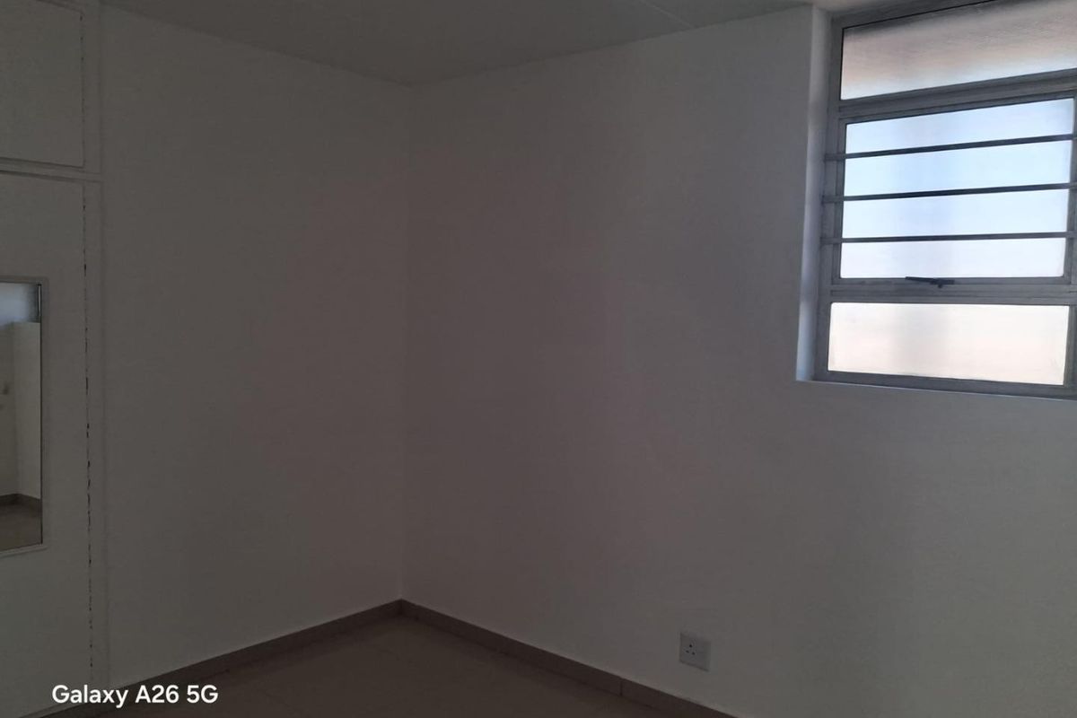 An empty bedroom featuring tiled flooring, a built-in cupboard, and a louvered window providing natural light.