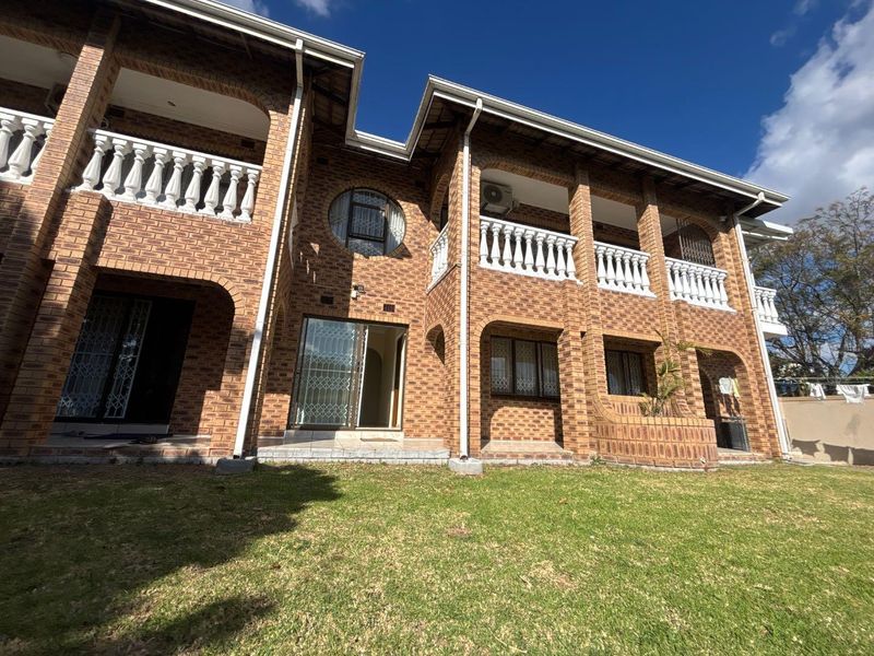 Rear view of a double-story face brick cottage featuring a spacious lawn, upper-level balconies with balustrades, and secure sliding door access.