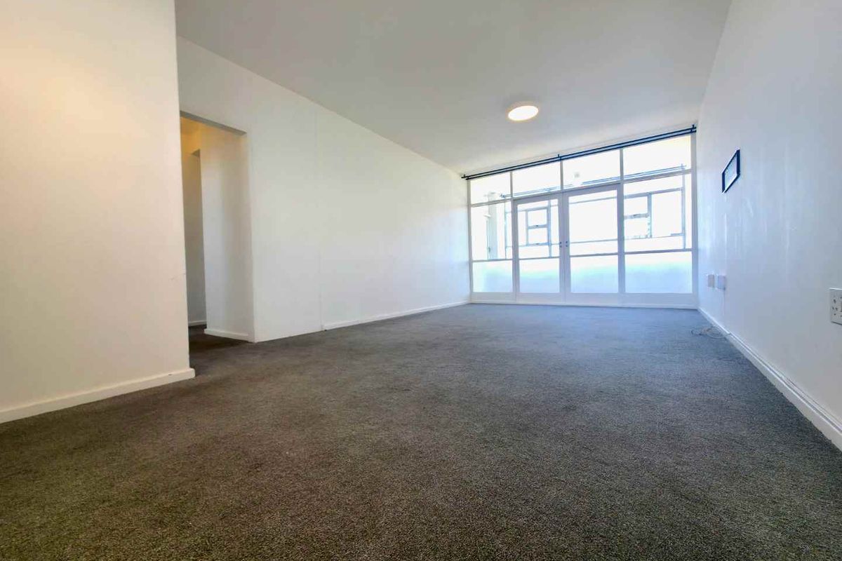 A spacious, empty living room featuring neutral carpeting, white walls, and large glass sliding doors providing ample natural light.