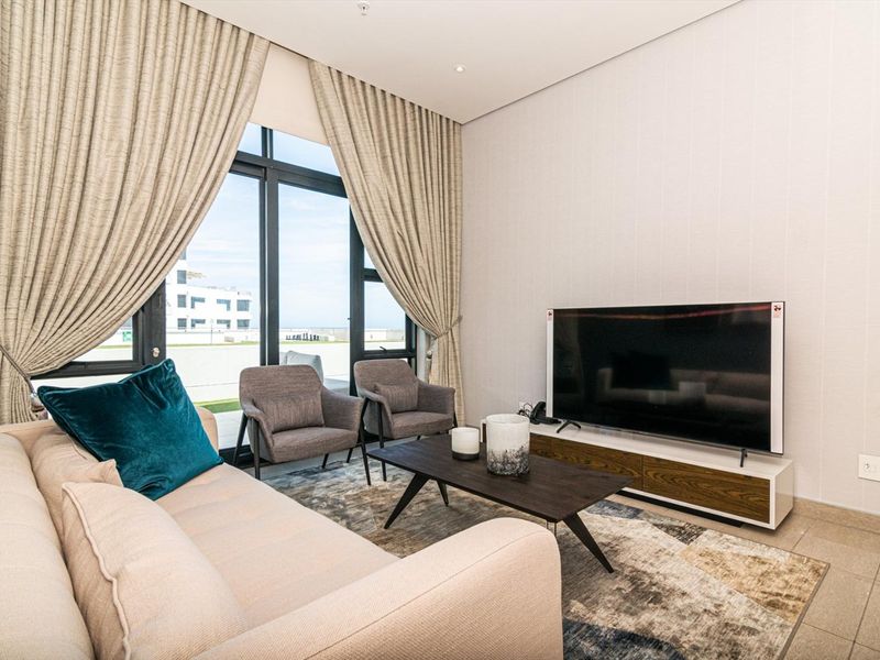 A modern, well-maintained living room featuring large floor-to-ceiling windows that provide ample natural light and a view of the exterior.