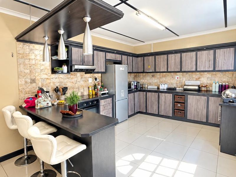Spacious kitchen featuring dark wood-grain cabinetry, stone tile backsplash, a breakfast bar with pendant lighting, and large ceramic floor tiles.