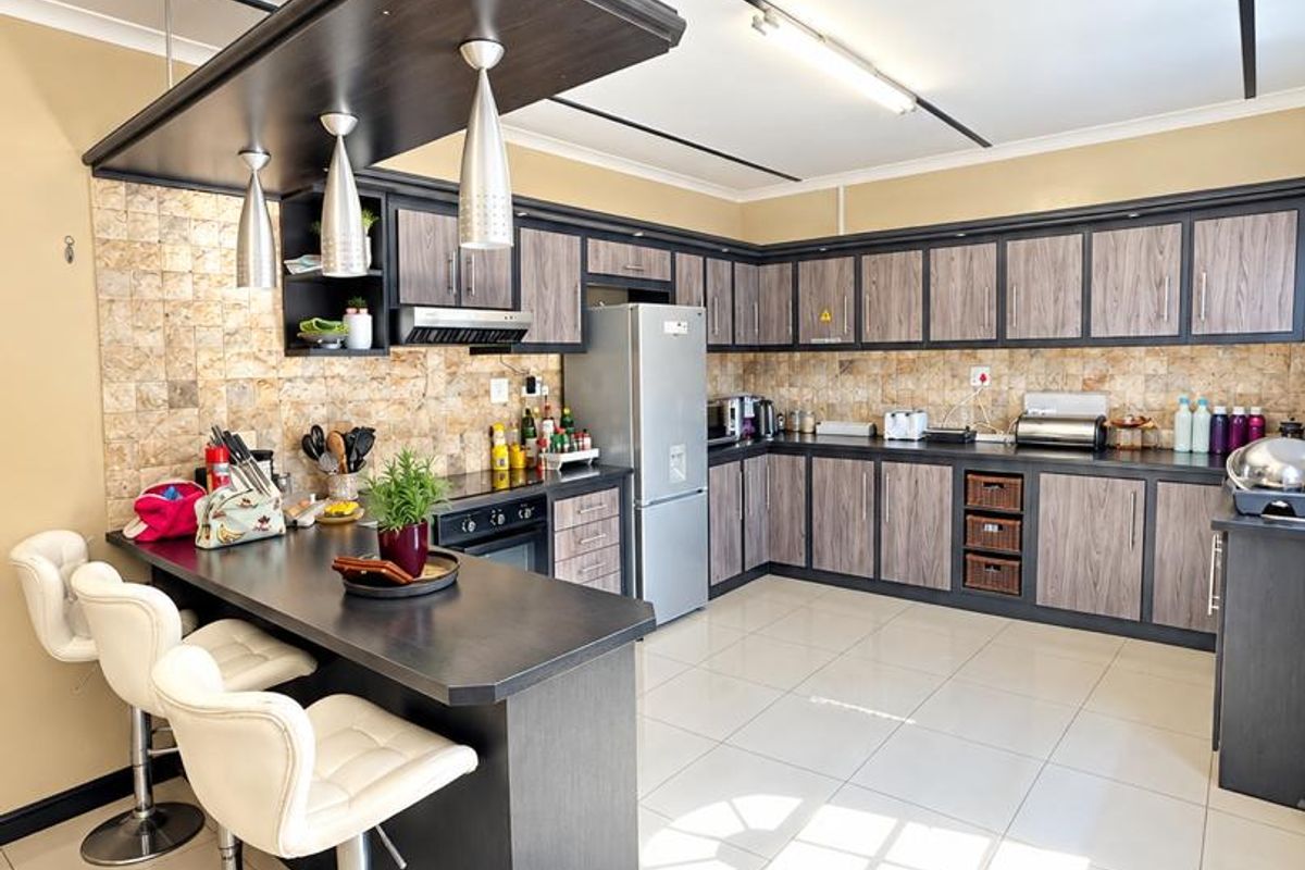 Spacious kitchen featuring dark wood-grain cabinetry, stone tile backsplash, a breakfast bar with pendant lighting, and large ceramic floor tiles.