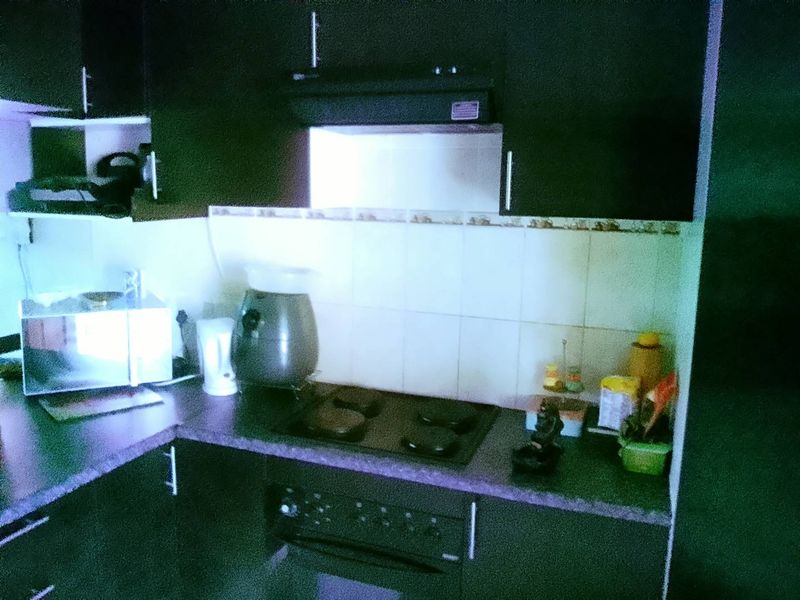 A compact kitchen featuring dark cabinetry, a tiled backsplash, and integrated cooking appliances including an electric hob and oven.