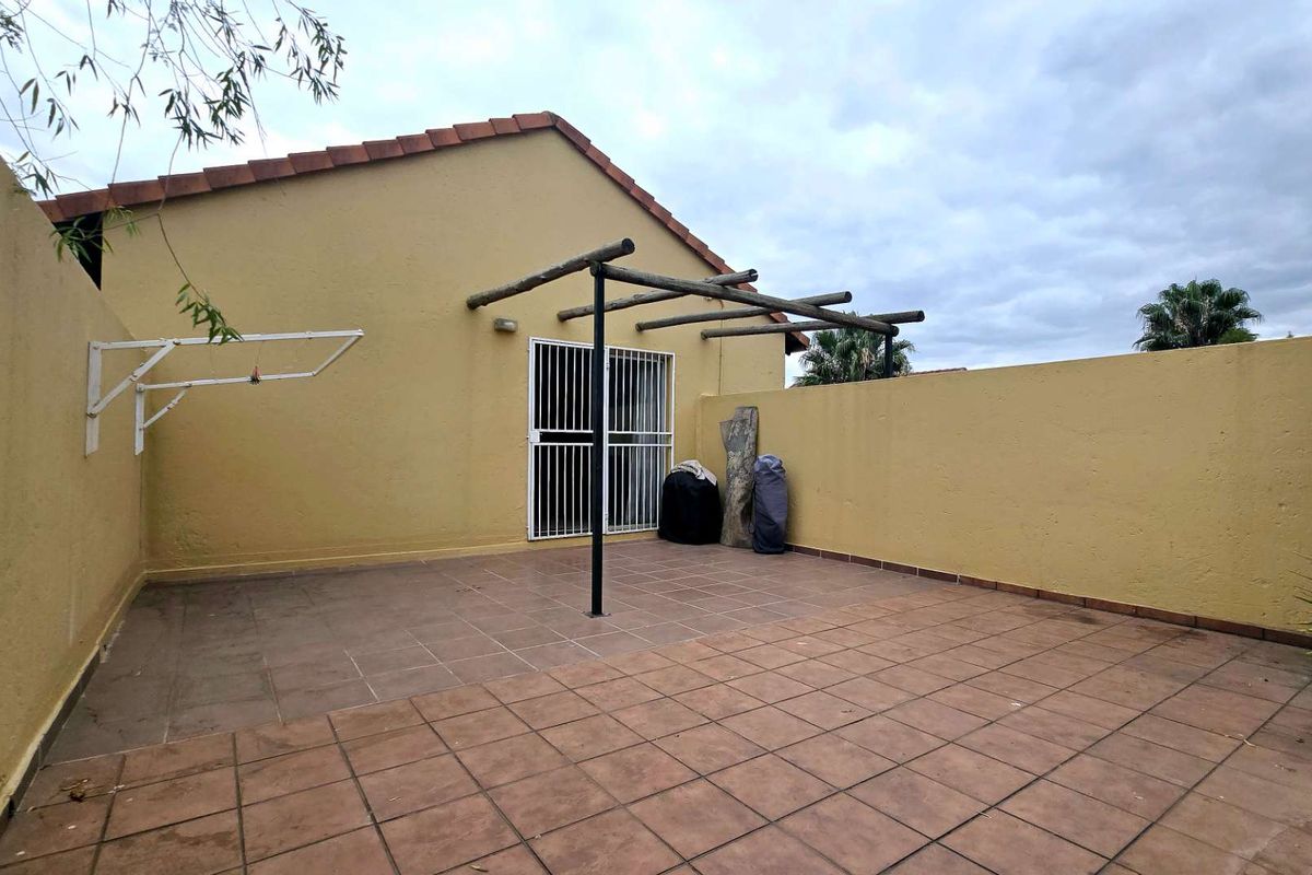 A private rear patio area featuring tiled flooring, a wooden pergola structure, and a wall-mounted drying rack, enclosed by high boundary walls.