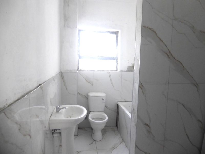 A compact bathroom featuring a pedestal basin, toilet, and bathtub with marble-look tiling, currently requiring finishing touches to the walls and grout.