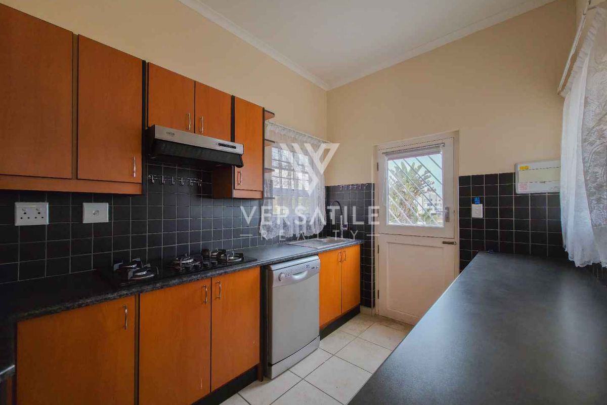 A functional kitchen featuring wooden cabinetry, dark countertops, a gas hob with extractor fan, and tiled flooring with direct access to the exterior.