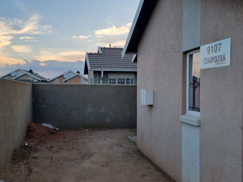 A view of the rear exterior area featuring a plastered facade, boundary wall, and an unlandscaped yard space.