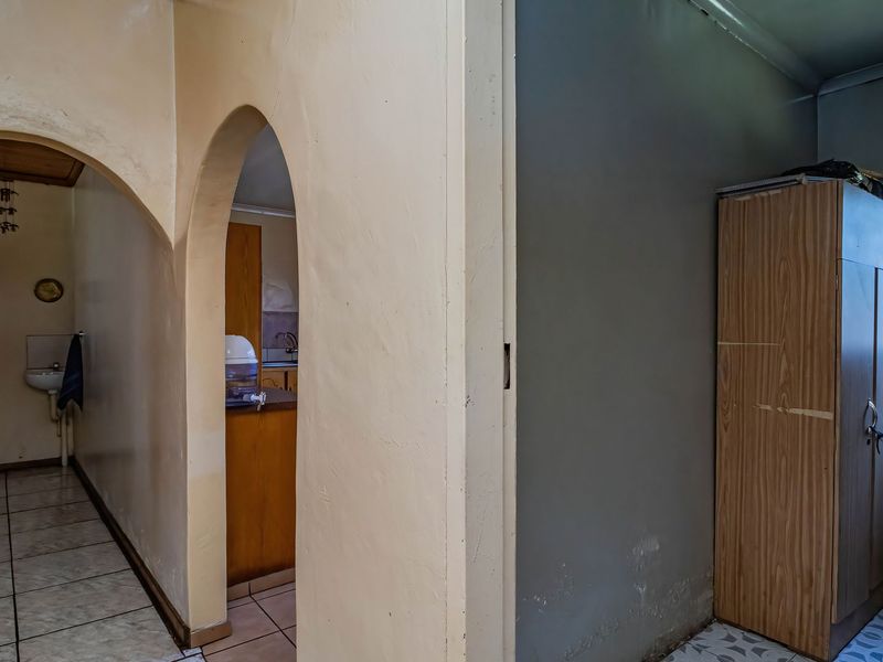 A hallway featuring arched architectural details, tiled flooring, and visible wear on the wall finishes requiring maintenance.