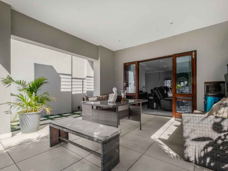 A covered patio area featuring large format floor tiles and timber-framed sliding doors providing seamless access to the interior living space.