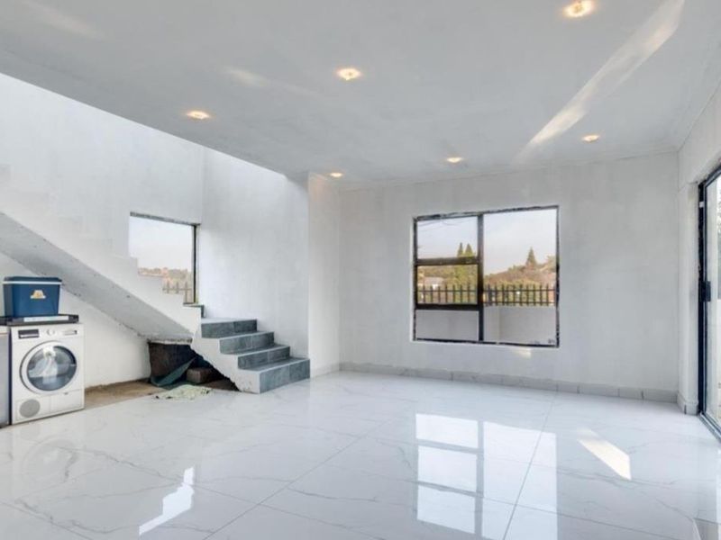 Spacious open-plan living area featuring large format white floor tiles, recessed lighting, and a modern staircase with access to outdoor space.