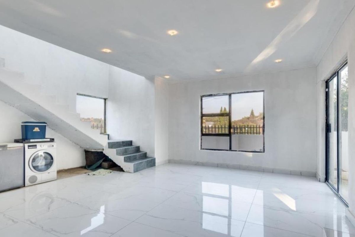 Spacious open-plan living area featuring large format white floor tiles, recessed lighting, and a modern staircase with access to outdoor space.