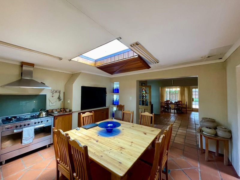 Open plan kitchen and dining area featuring terracotta flooring, a central skylight, and built-in cabinetry, showing signs of ceiling wear and dated finishes.