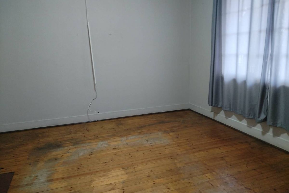 An empty bedroom featuring original timber flooring and a window with curtains, requiring cosmetic updates to the floor and wall finishes.