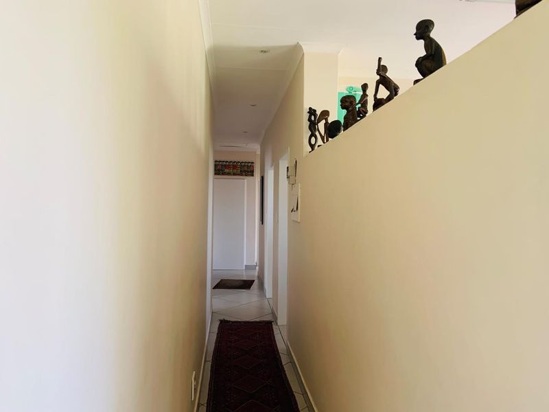 A narrow residential hallway featuring tiled flooring, recessed downlighting, and a coved ceiling, providing access to various rooms within the apartment.