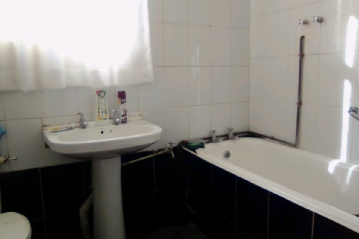 A functional bathroom featuring a pedestal basin and bathtub with tiled finishes. The space would benefit from modernization and improved plumbing concealment.