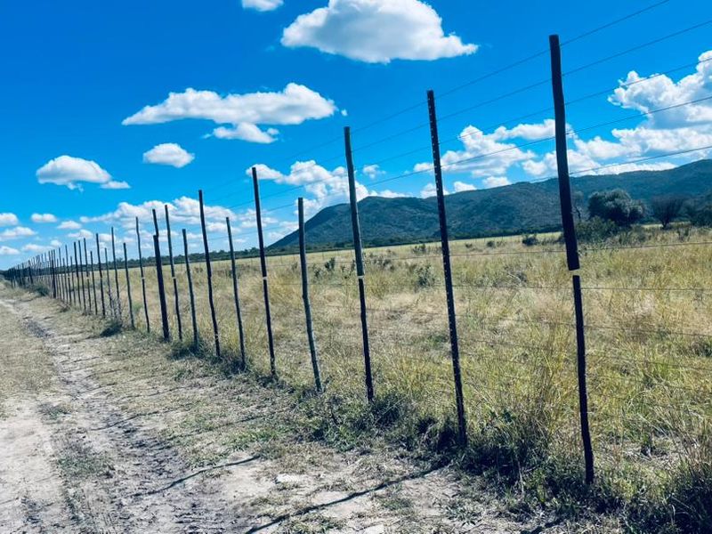 Expansive rural landscape view featuring a long stretch of wire fencing along a dirt track with mountain vistas in the background.