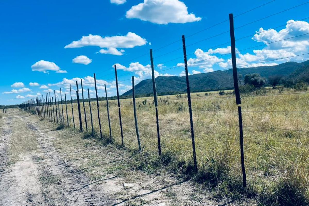 Expansive rural landscape view featuring a long stretch of wire fencing along a dirt track with mountain vistas in the background.