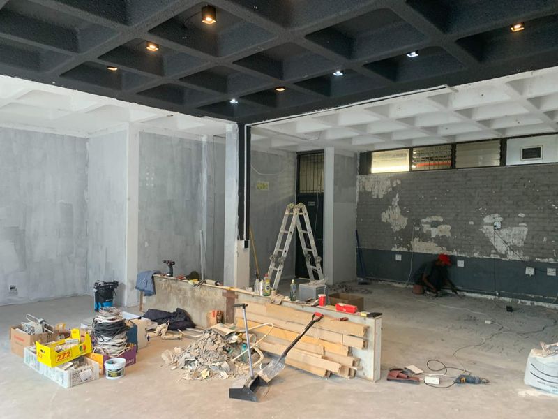 An open-plan retail space currently undergoing renovation, featuring a distinctive coffered ceiling, recessed lighting, and exposed brickwork awaiting final finishes.