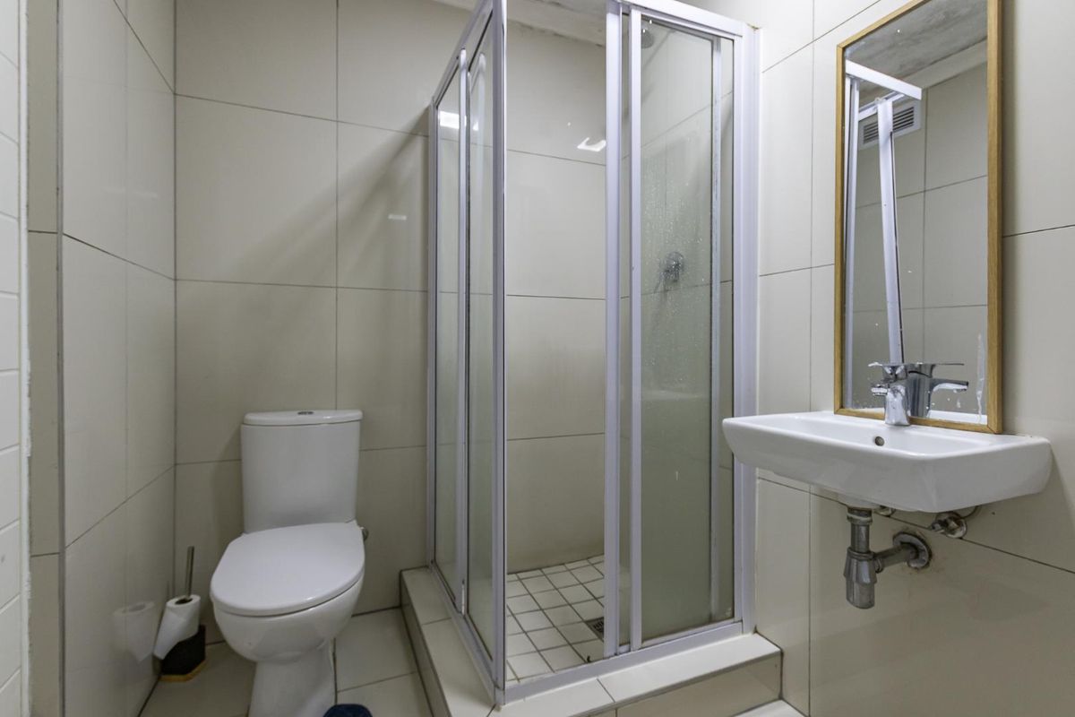 A compact bathroom featuring a tiled shower enclosure, a wall-mounted basin with a mirror, and a standard toilet.