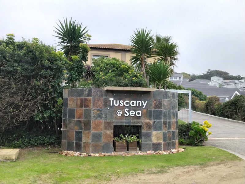 Entrance view of the Tuscany @ Sea estate, featuring a stone-clad signage wall, landscaped garden, and paved driveway access.