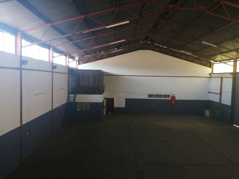 Spacious industrial warehouse featuring high ceilings with exposed steel trusses, concrete flooring, and a mezzanine level suitable for office or storage use.