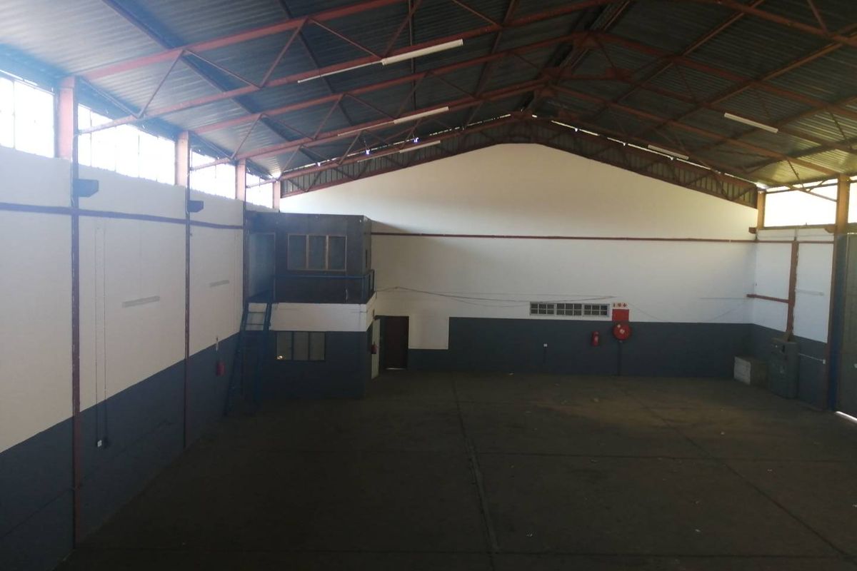 Spacious industrial warehouse featuring high ceilings with exposed steel trusses, concrete flooring, and a mezzanine level suitable for office or storage use.