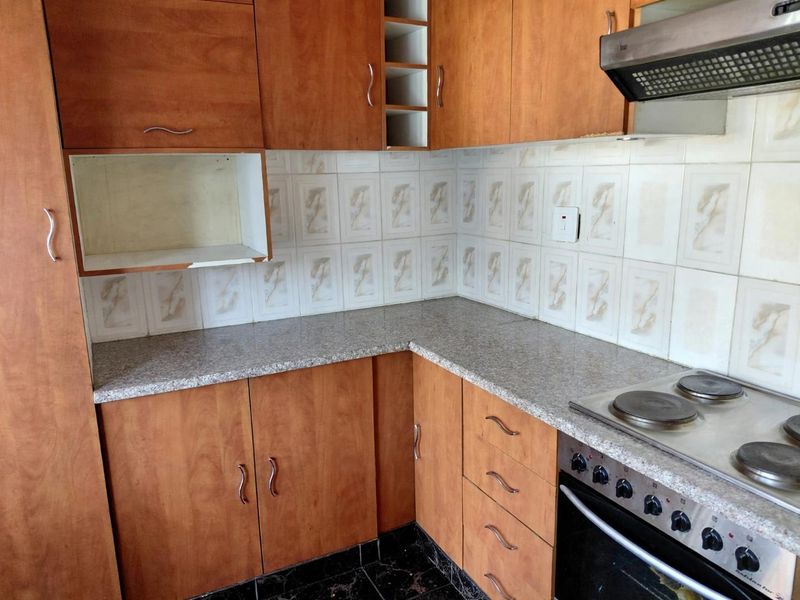 A functional kitchen featuring wood-look cabinetry, granite-style countertops, a built-in electric oven with hob, and a tiled backsplash.