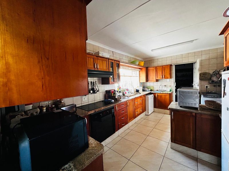 A functional kitchen featuring wooden cabinetry, laminate countertops, built-in oven, electric cooktop, and tiled flooring, offering a classic layout with ample storage space.