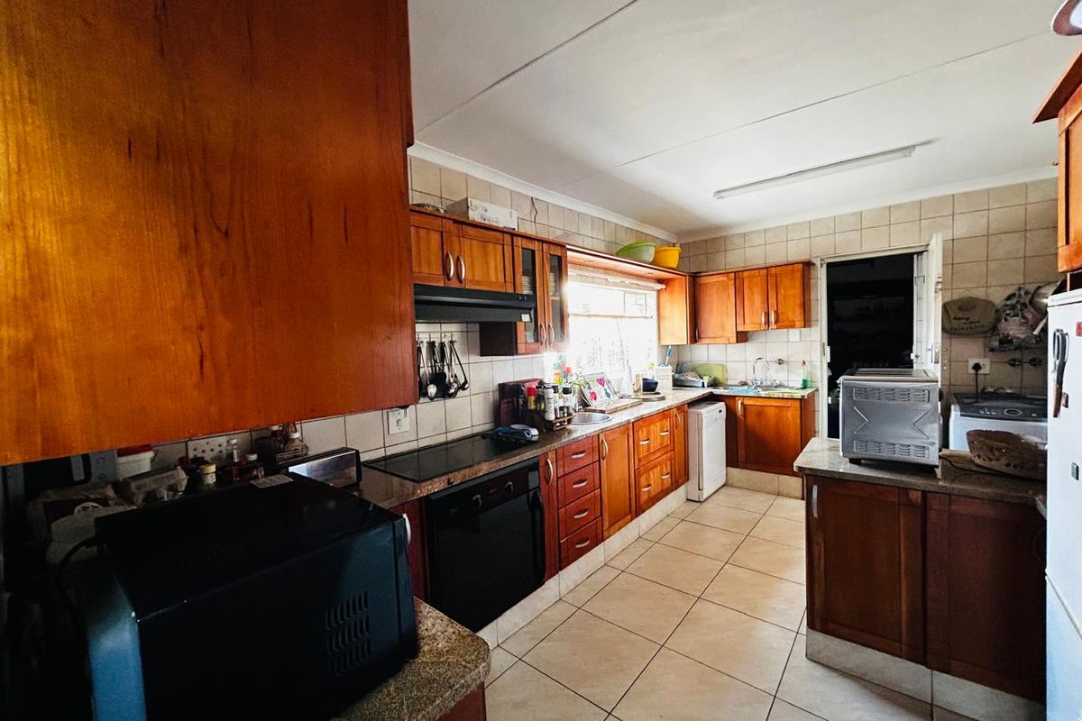 A functional kitchen featuring wooden cabinetry, laminate countertops, built-in oven, electric cooktop, and tiled flooring, offering a classic layout with ample storage space.