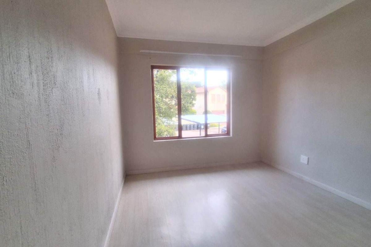 A vacant bedroom featuring light-toned laminate flooring, neutral walls, and a timber-framed window providing natural light.