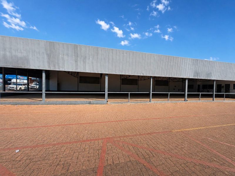 Front exterior view of a commercial property featuring a paved parking area, covered walkway, and metal facade cladding.