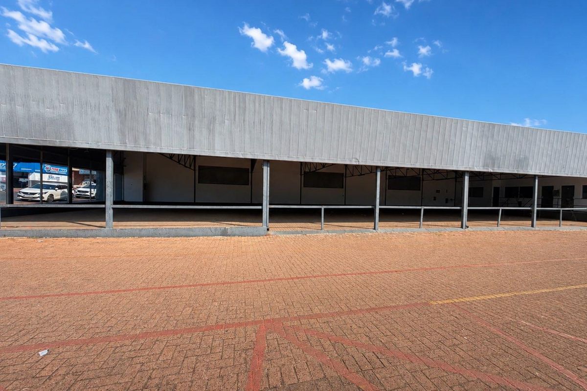 Front exterior view of a commercial property featuring a paved parking area, covered walkway, and metal facade cladding.